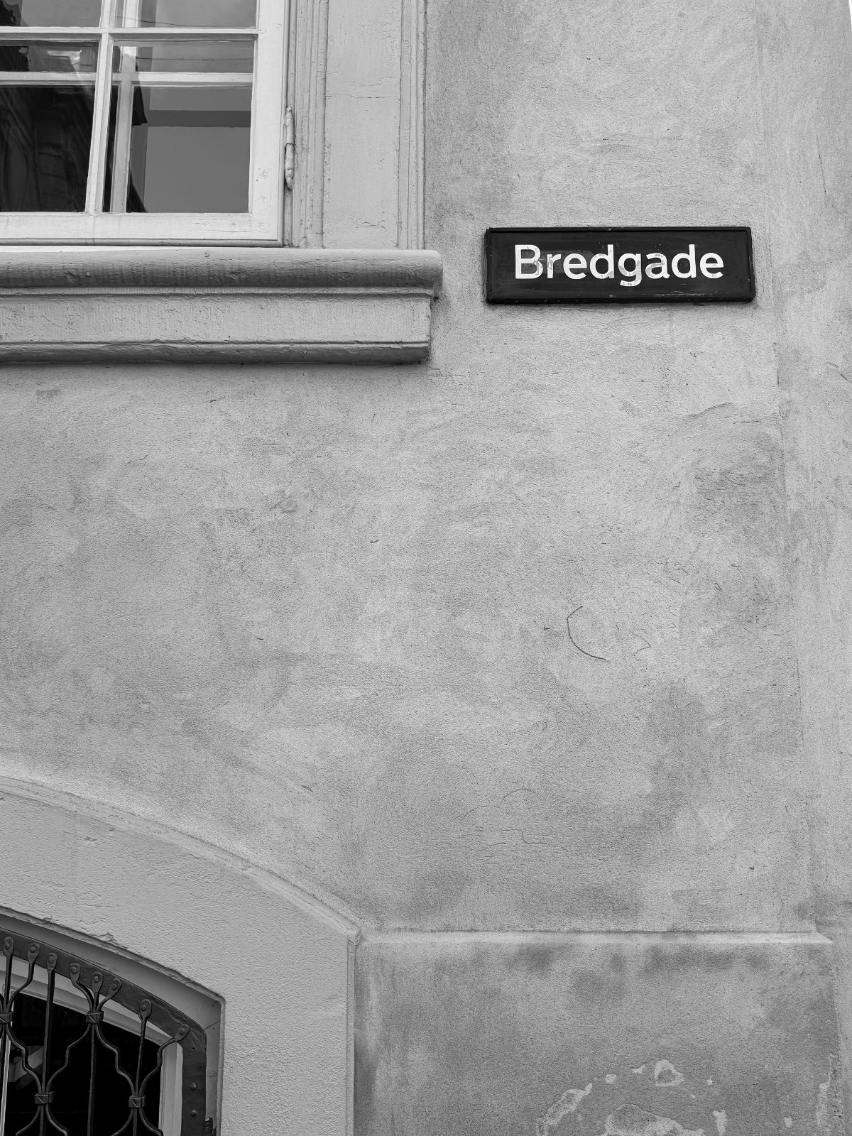 Bredgade street sign on a plastered facade — black and white